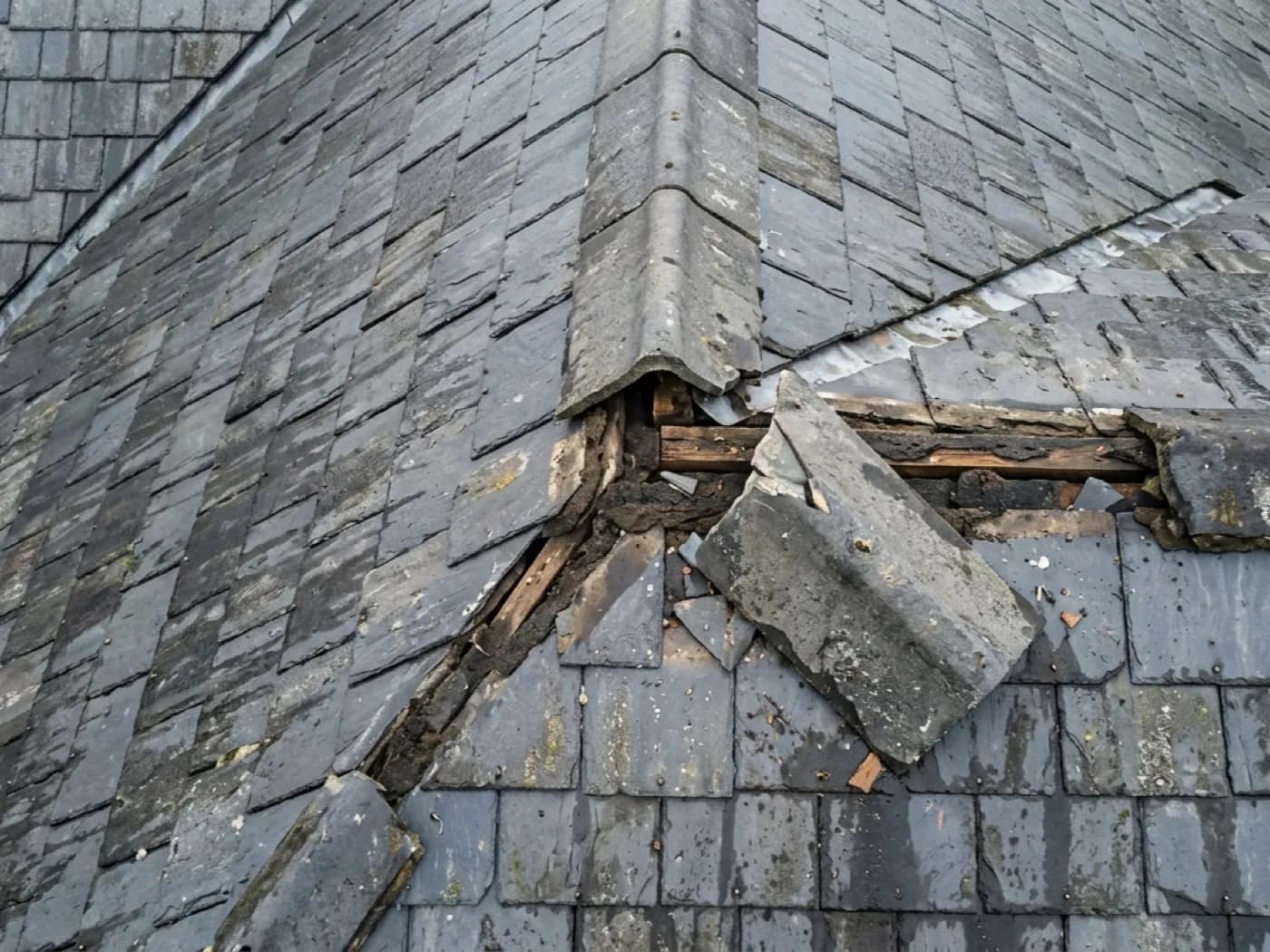 A lifted and displaced ridge tile on a slate roof after a storm, photographed from directly above